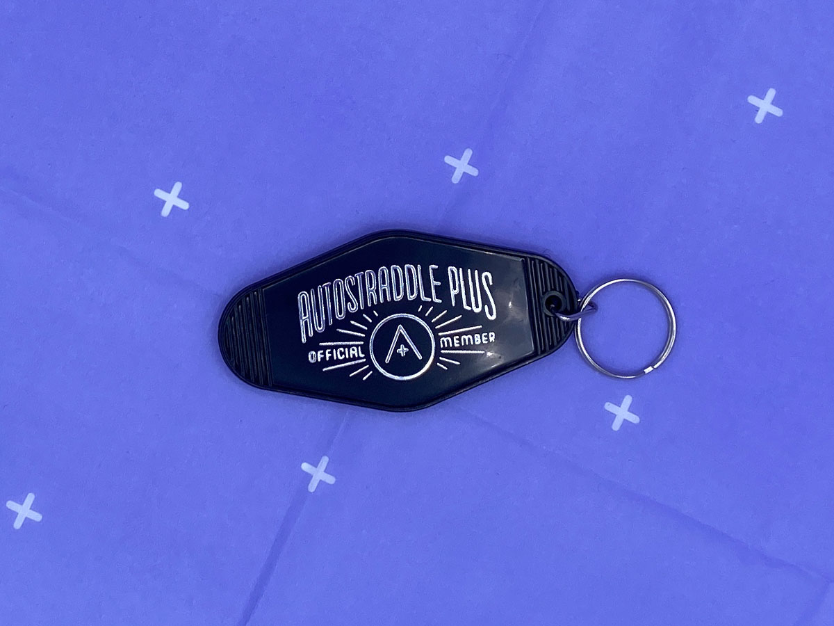 a black motel style keychain with silver imprint that says Autostraddle Plus Official Member, with the A+ logo surrounded by a halo of lines