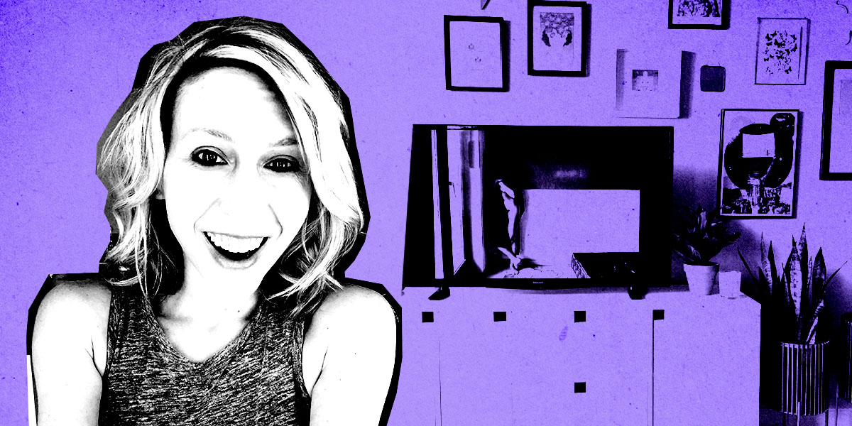Riese is smiling, in high contrast in front of a background showing her TV and wall of art. the image is in black and white and purple.