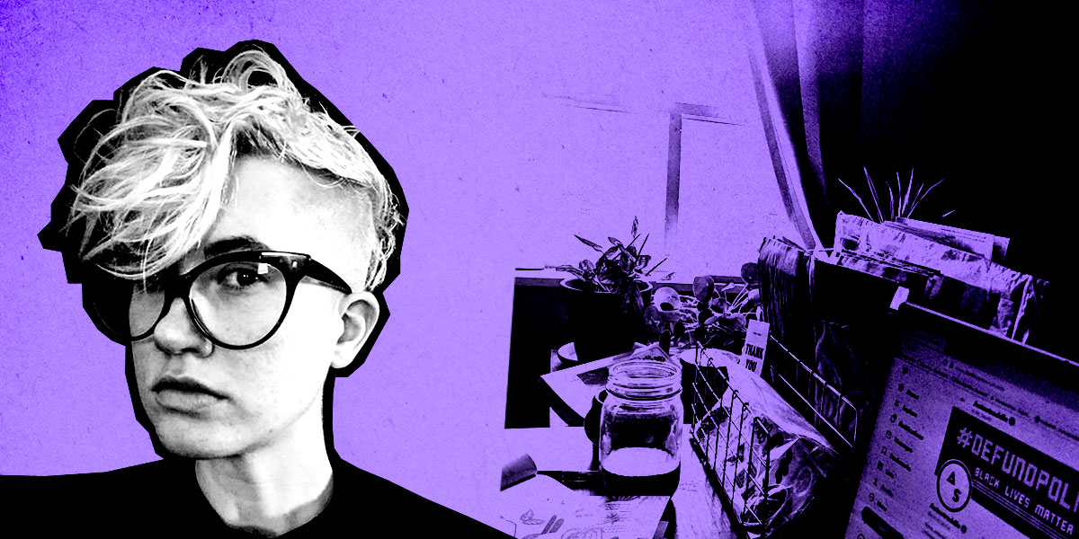 Nicole (a white, non-binary human with bleached hair and shaved sides, large dark glasses) in front of a purple background with their desk behind them.