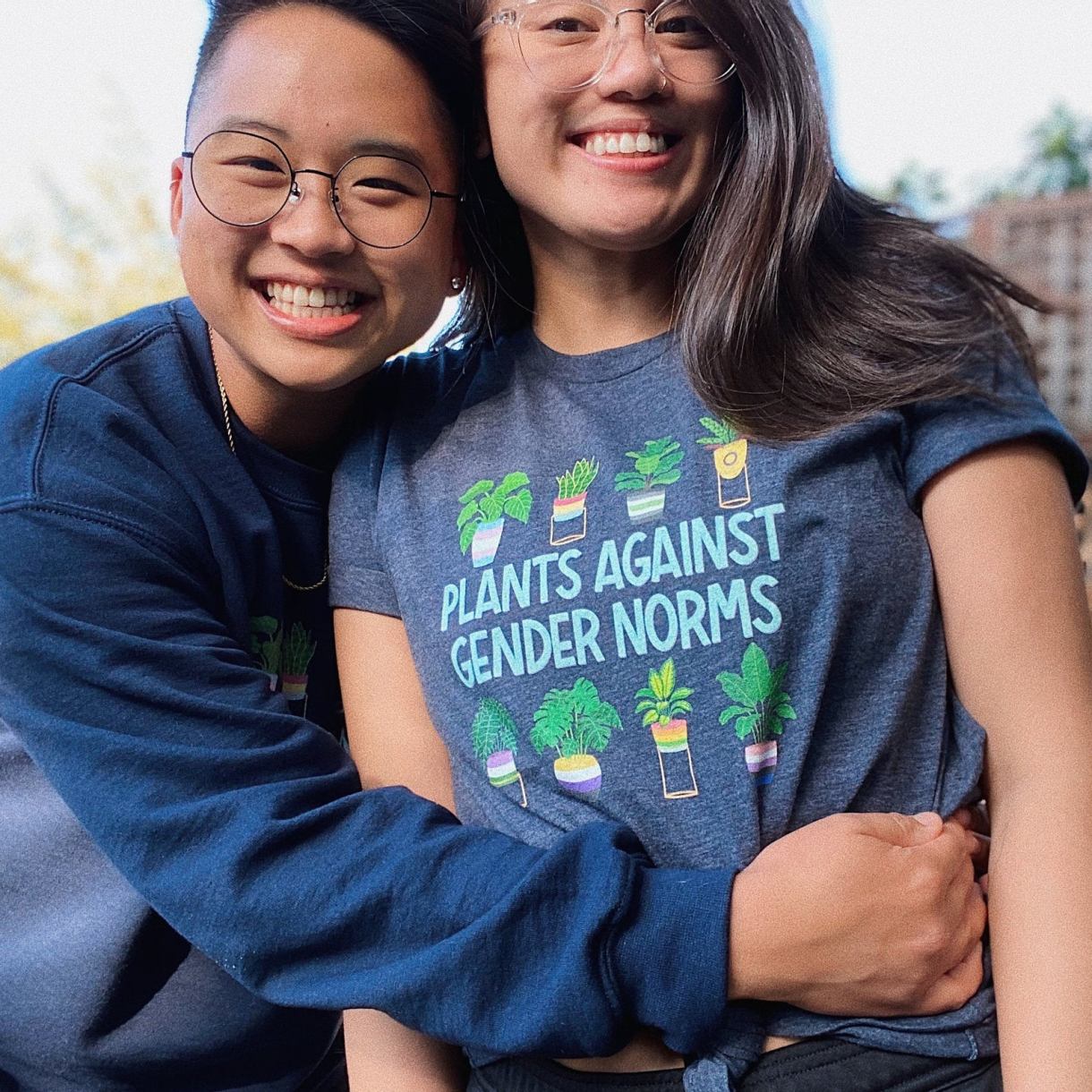 The artist hugging a model wearing a "Plants Against Gender Norms" t-shirt that has pictures of house-potted plants above and below the slogan.