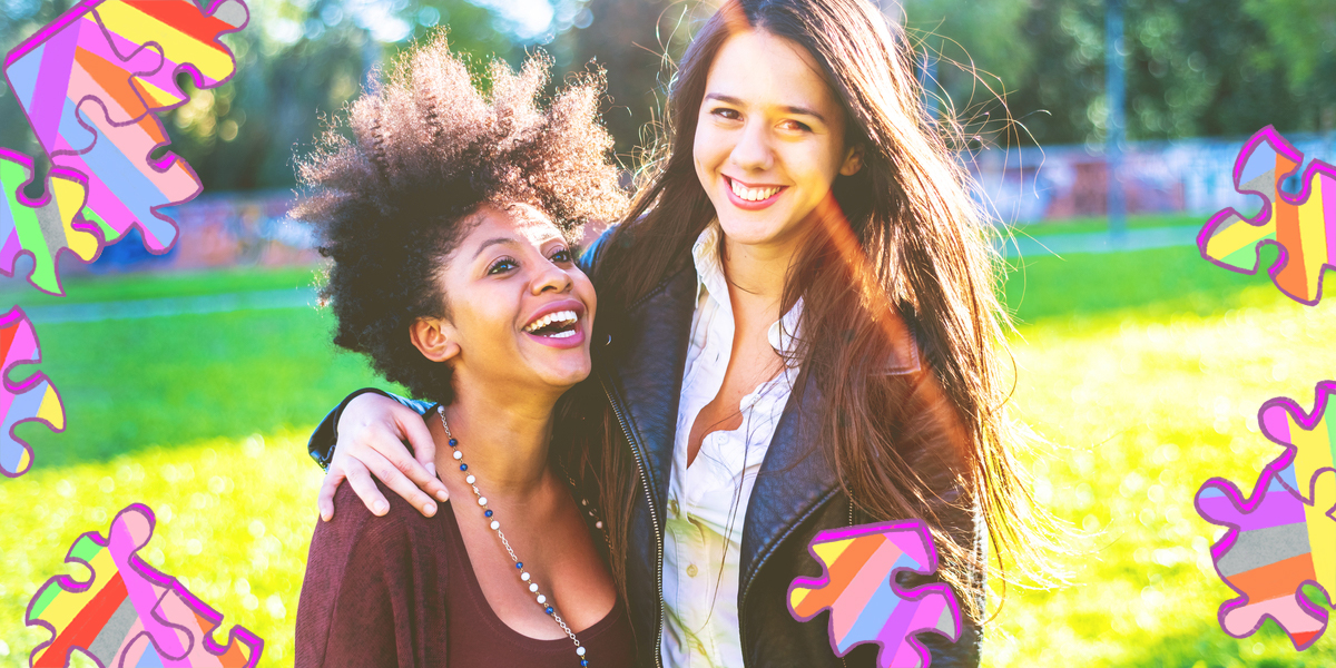 Two women with their arms around each other are standing in a sunny park. One woman has natural hair and a scoopneck shirt, the other is wearing a button-up and leather jacket with straight hair.
