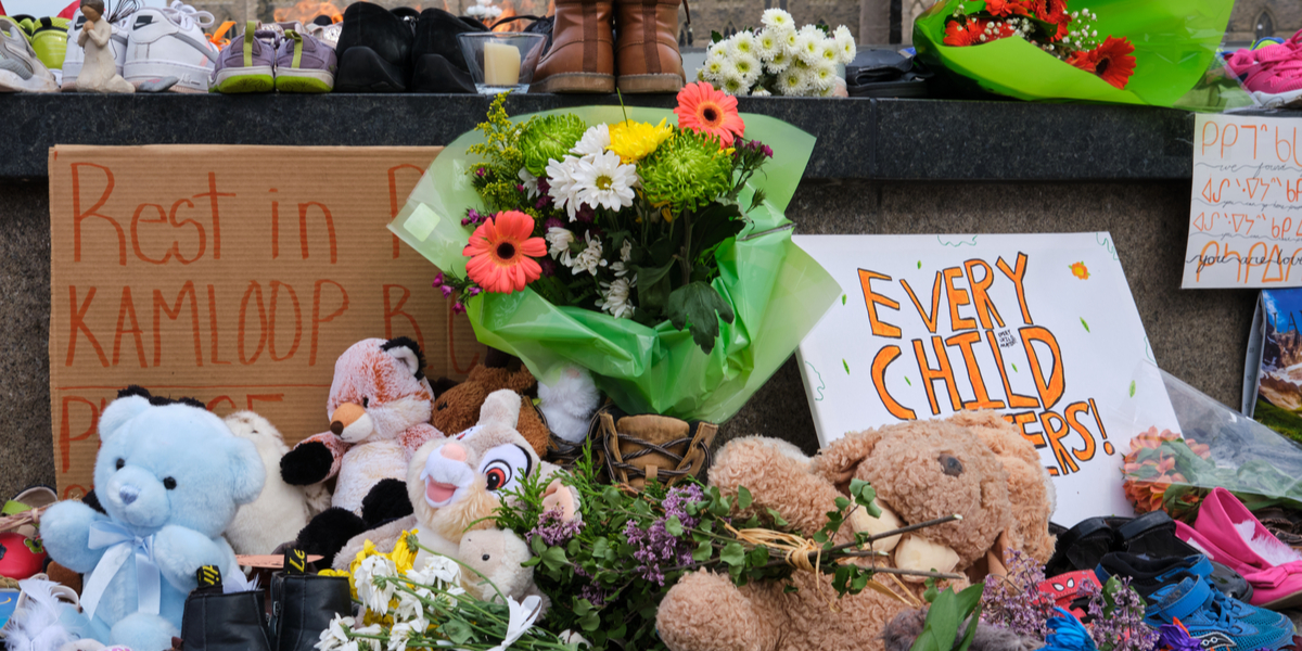 A memorial assembled for children found at Kamloops Residental School, featuring flowers, stuffed animals and children's toys, as well as signs that read REST IN PEACE KAMLOOPS and EVERY CHILD MATTERS