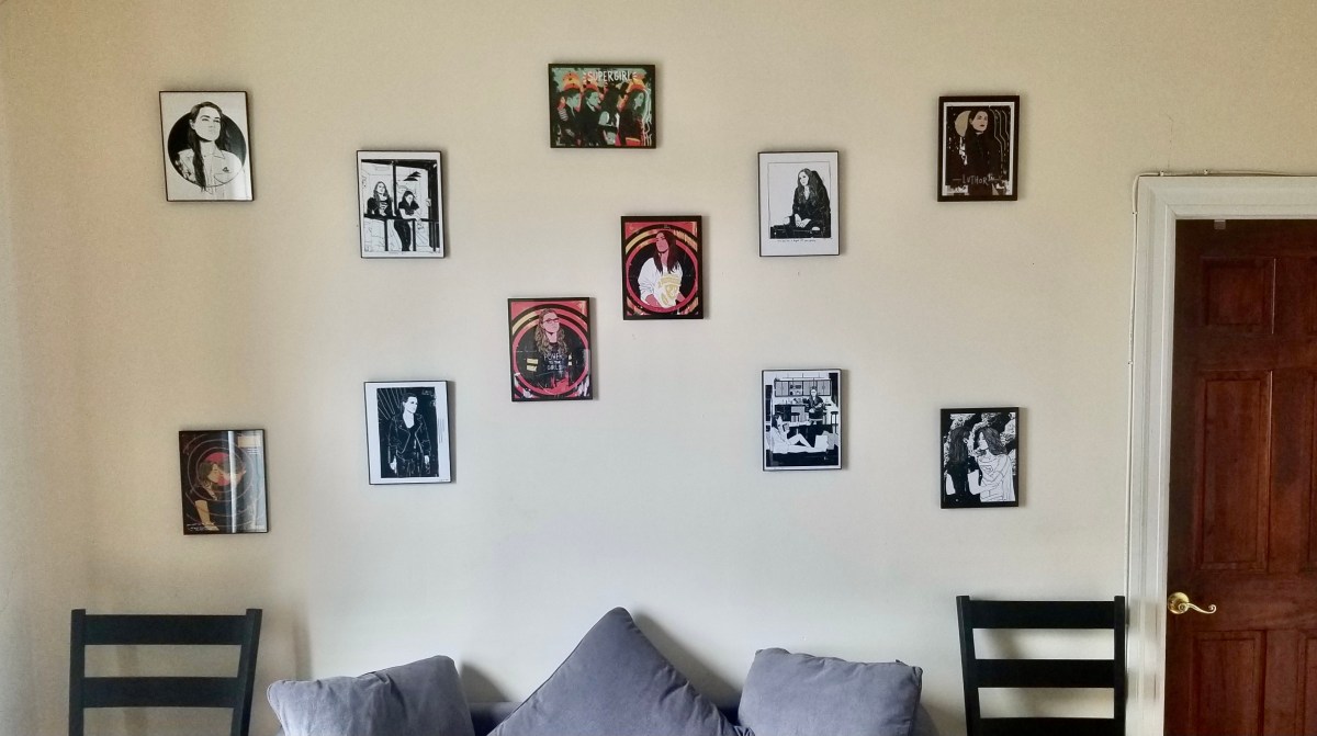 Framed fan art hung in X pattern on beige wall, over a sofa and two chairs