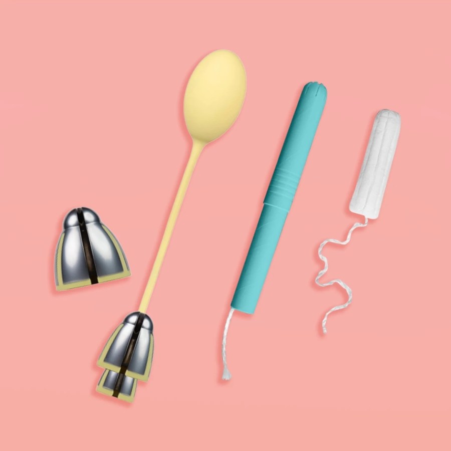 A product photo of the Kegelbells set, two metal weights and a silicone connector to hold them together, shown next to a tampon and tampon applicator as a size comparison.