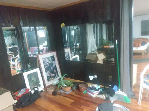 a room with some framed pictures on the floor, leaning against the wall, a little bit of clutter on the floor, and mirrors on the walls.