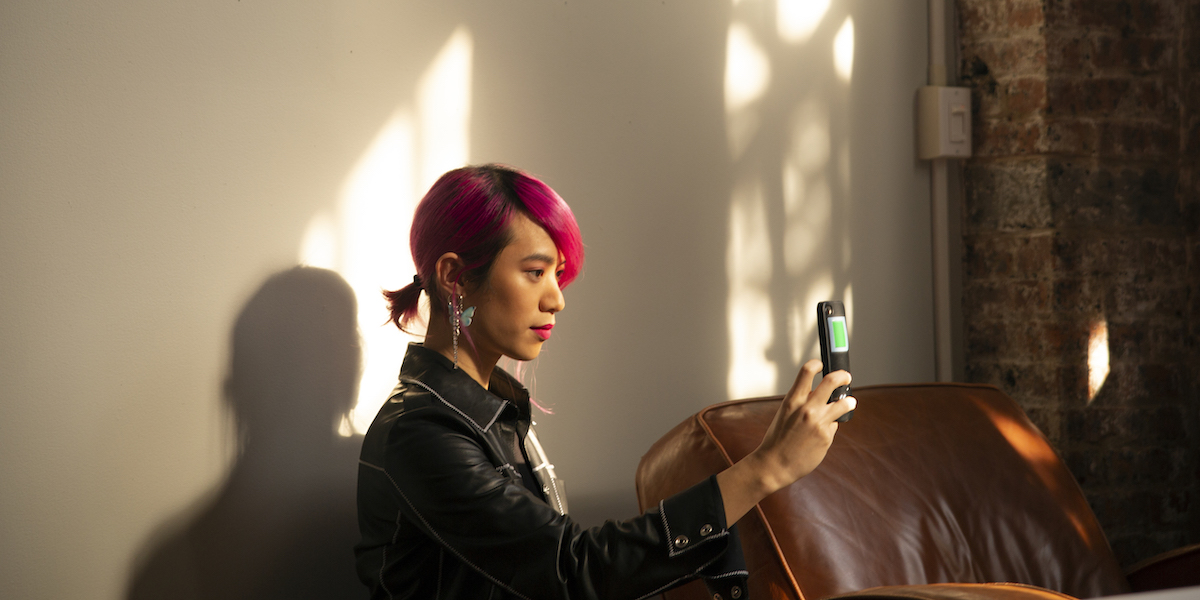 A person with pink hair in a short ponytail takes a selfie with their phone in a sunlit loft. Photo by Zackary Drucker as part of Broadly's Gender Spectrum Collection. Credit: The Gender Spectrum Collection. Made available to media outlets via Creative Commons.