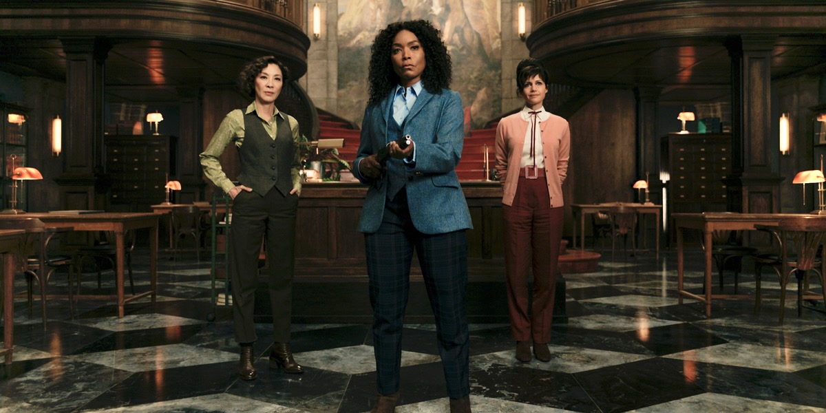 In this review for Gunpowder Milkshake, Angela Bassett has on a blue suit and holds a firearm, Michelle Yeoh and Carla Gugino are behind her.