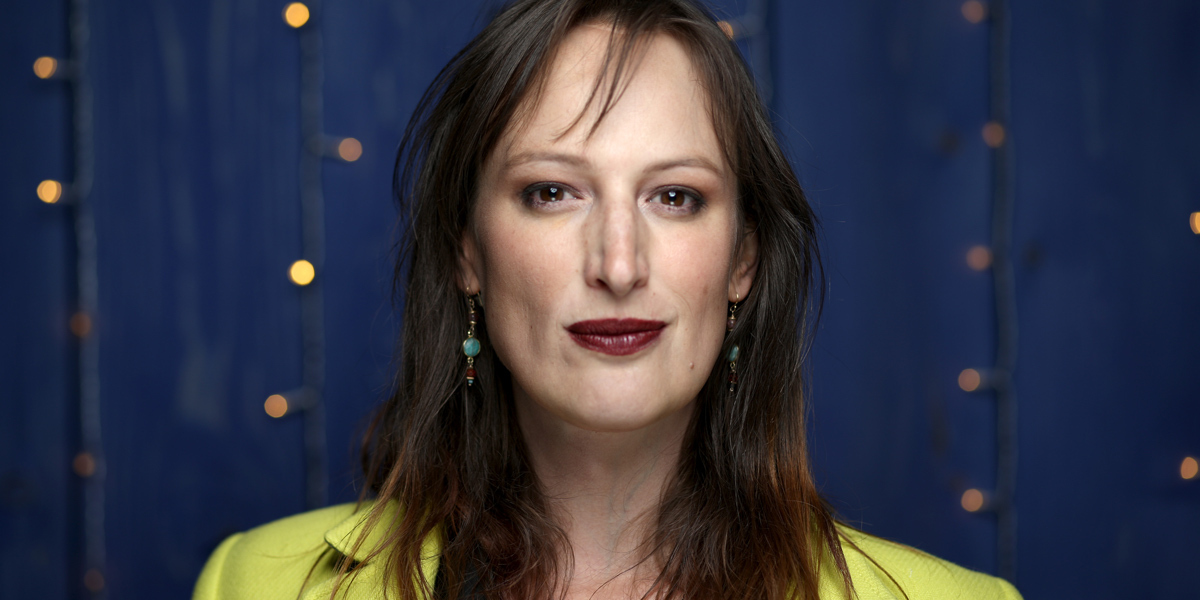 Jen Richards interview: Jen Richards in a chartreuse top and dark lipstick against a navy blue background
