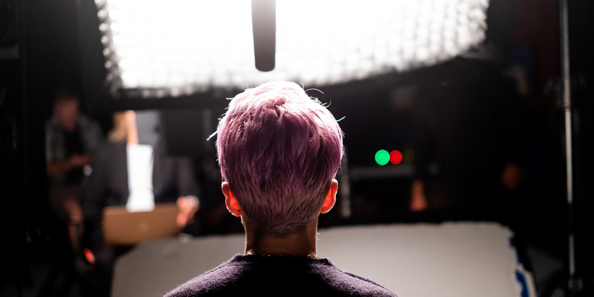 LFG Review: The back of Megan Rapinoe's head is backlight against a bright camera light with a microphone hanging in front of her.