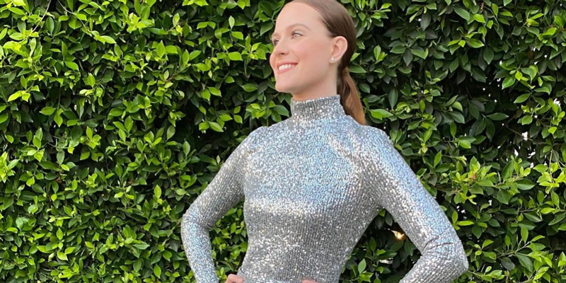 Evan Rachel Wood is in a sparkly silver gown in front of a green leafy wall, her hair is in a low slick ponytail.