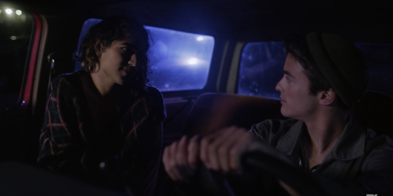 Dee played by Ben J. Pierce looks longingly at a cis boy next to them in a car.