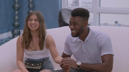 Image shows a Black man holding the hand of a brunette white woman while they both laugh and smile.