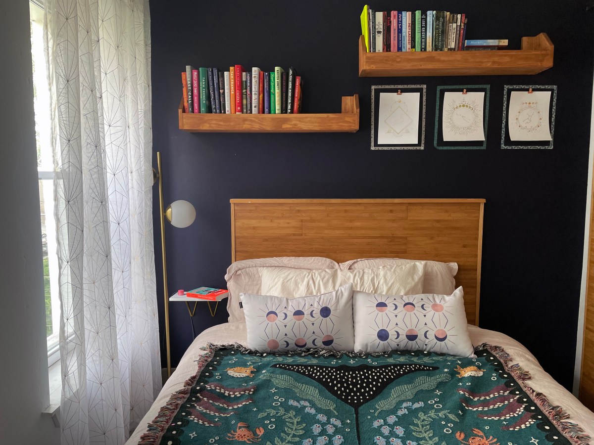 a bed with a mermaid throw on top of it, bookshelves and a gold lamp