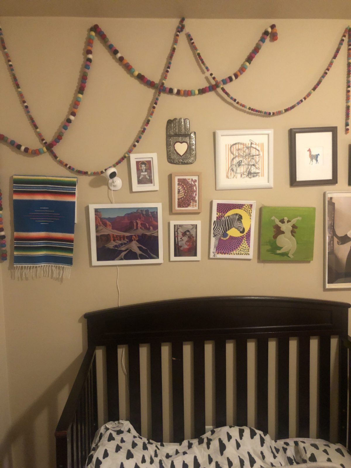 Strings of beads hung in cascades on a beige wall, hung above a variety of framed prints and drawings, with a dark wooden headboard below