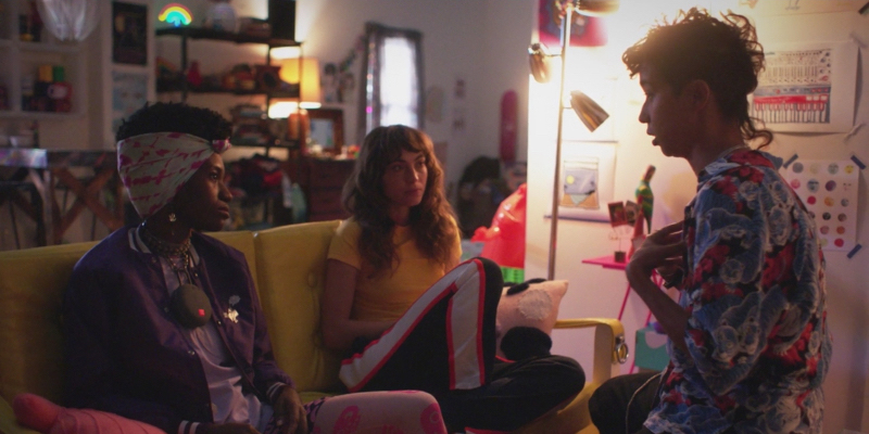 Victoria talks to Honeybear and Ash who are next to each other on a yellow couch