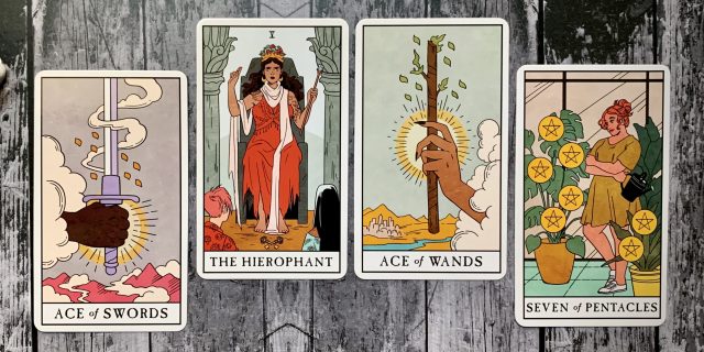 A spread of four tarot cards - the Ace of Swords, the Hierophant, Ace of Wands, and Seven of Pentacles - spread out against a wooden background