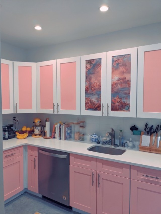 Kitchen with cabinets painted pink with white trim, and one set of panels with floral wallpaper