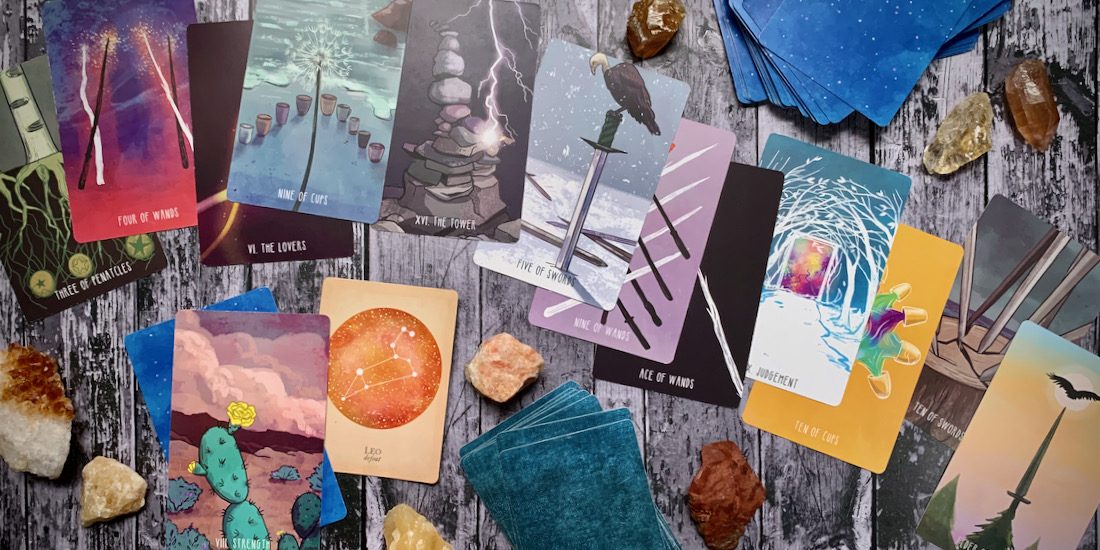 A scattered pile of beautiful brightly colored tarot cards and crystals across a wooden surface.