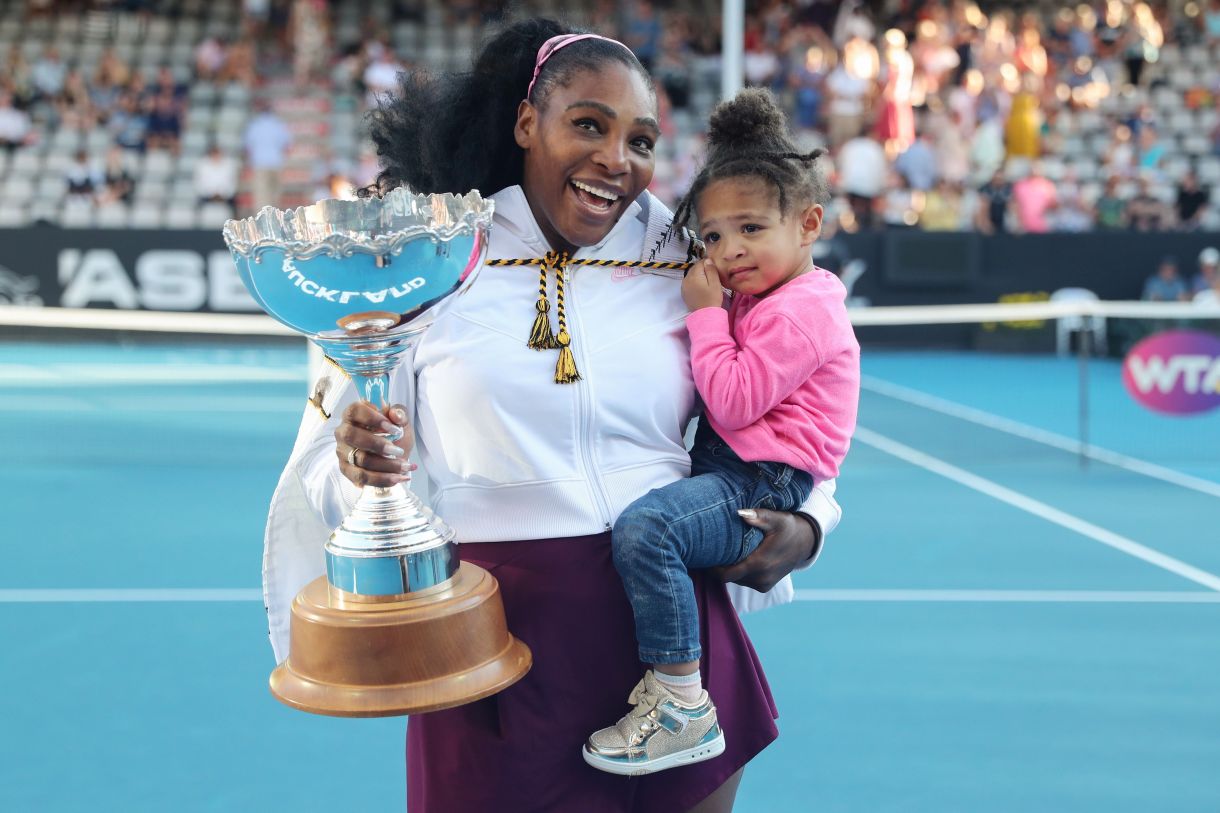 Serena Williams, the greatest athlete of all time, holding a trophy in one hand and her daughter in the other