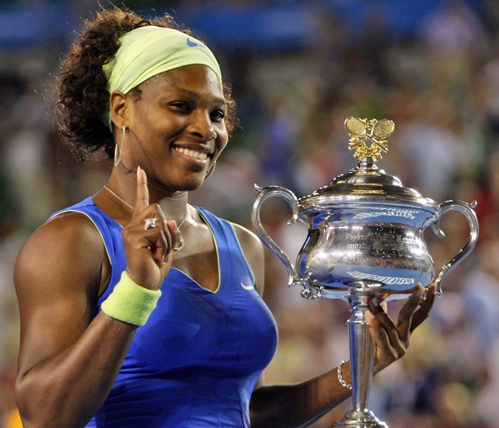 Serena Williams, the greatest athlete of all time, holding a single finger aloft with one hand with a trophy in the other hand