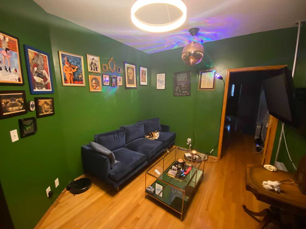 Living room with green walls, warm hardwood floors, a blue couch, and prints in a line around the wall