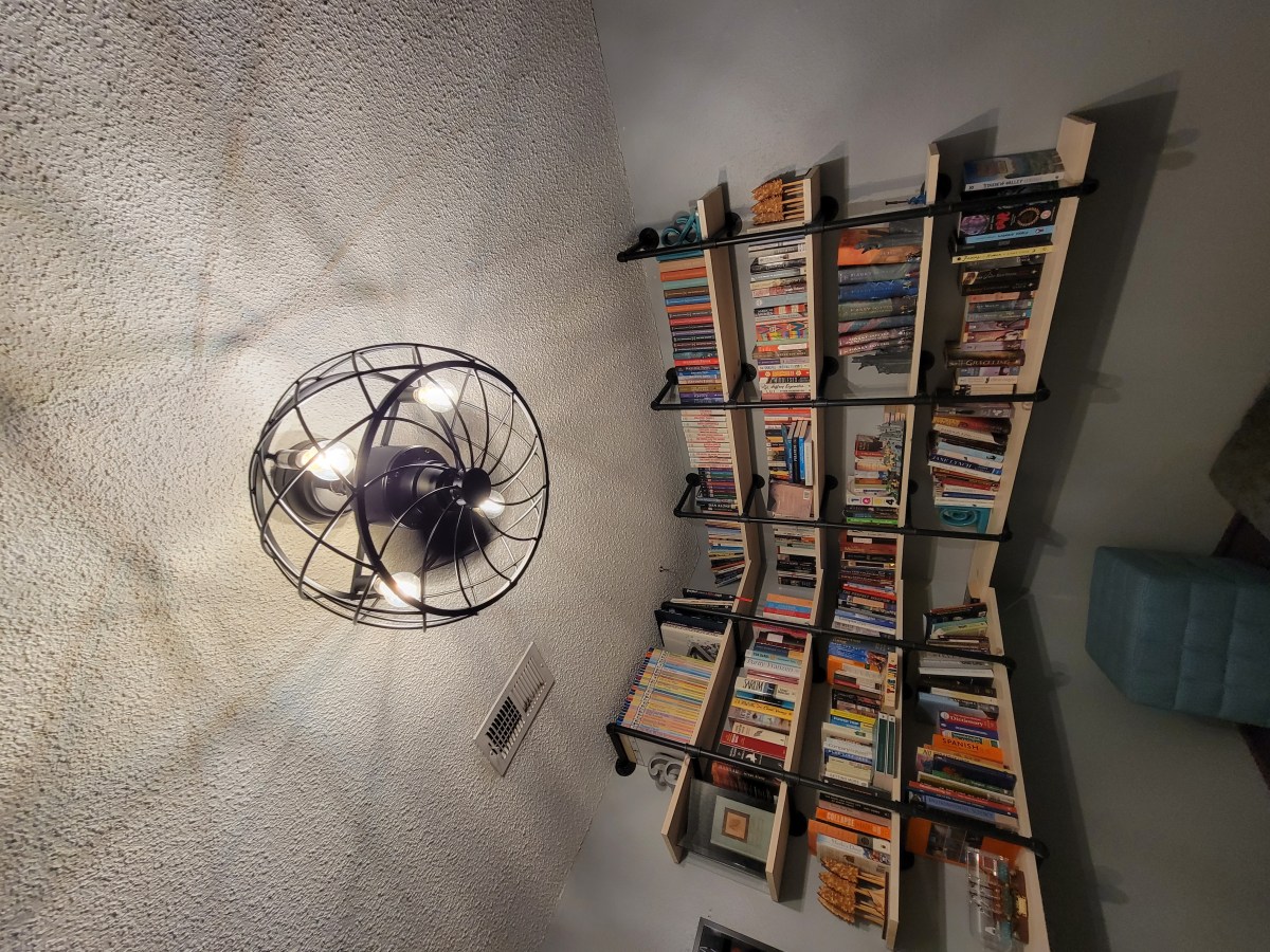 A large bookcase is mounted on the wall filling both angles of a corner, with a decorate lamp on the ceiling