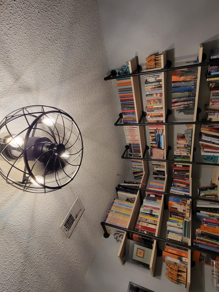 A large bookcase is mounted on the wall filling both angles of a corner, with a decorate lamp on the ceiling