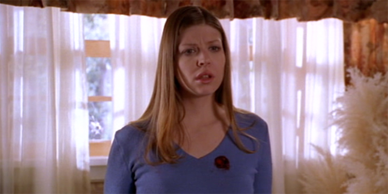 Tara Maclay of Buffy the Vampire Slayer stands in front of a window with a shocked look on her face and a bullet hole over her heart