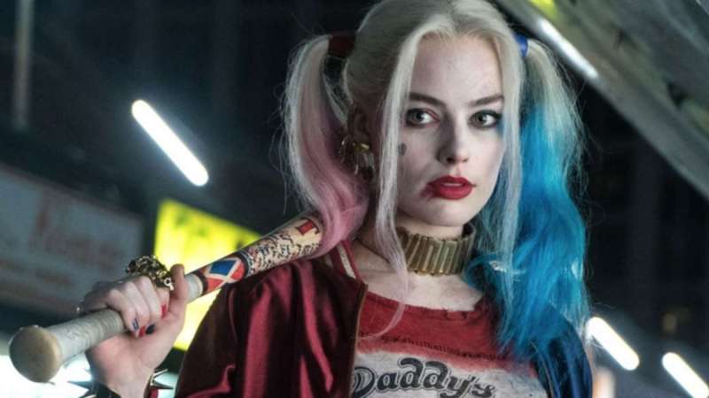 Harley Quinn holds a baseball bat behind her back, her hair is in pink and blue ponytails
