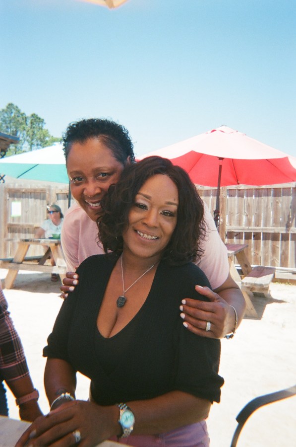 Rachel and Sheila Smallman, owners of lesbian bar Herz, pose together in a sunny outdoor location. They are both smiling.