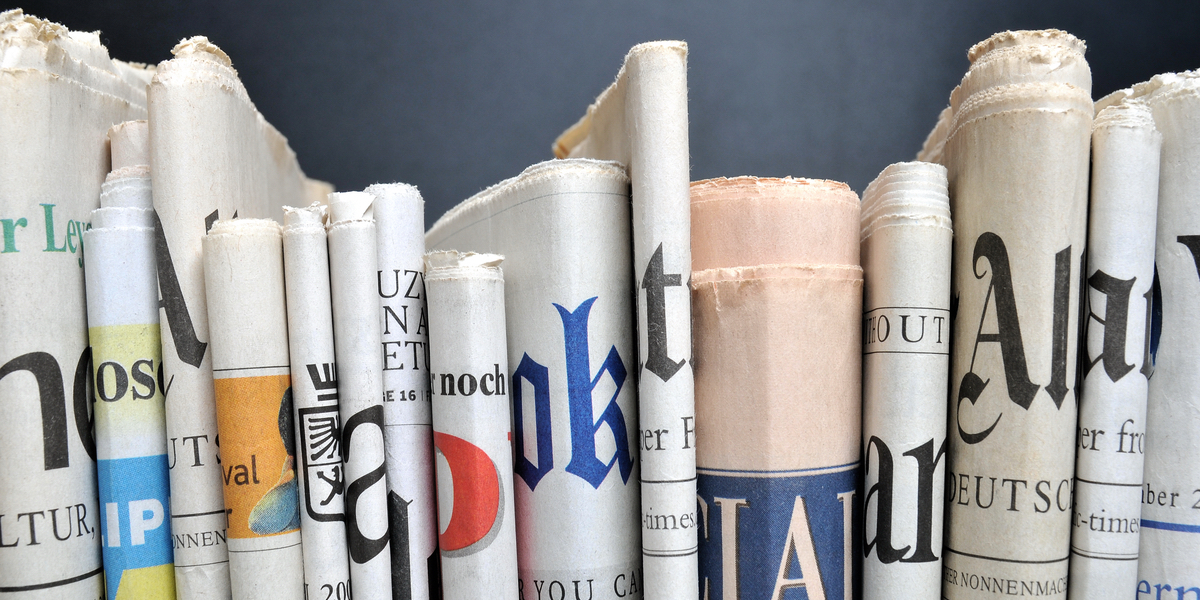 A close up of a variety of newspapers piled together horizontally.