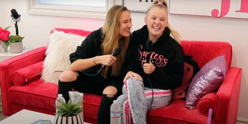 Jojo Siwa sits on a couch laughing with her girlfriend Kylie