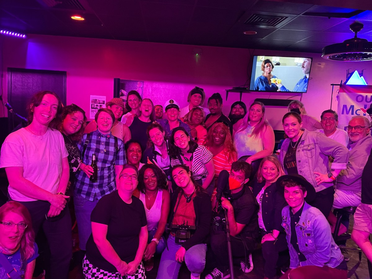 A huge group gathers at Herz, a lesbian owned bar in Mobile, Alabama. Everyone is smiling and looks happy.