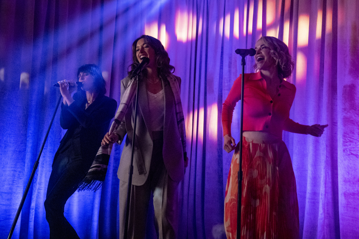 Shane, Bette and Alice from the L Word Gen Q sing karaoke on a stage lit with bisexual lighting