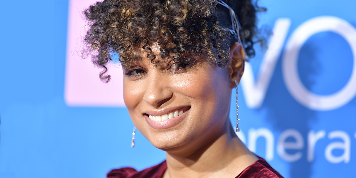 Rosanny Zayas smiles at the camera on the premiere of The L Word: Generation Q, she has thin dangly earring and her curls piled on top of her head in an updo