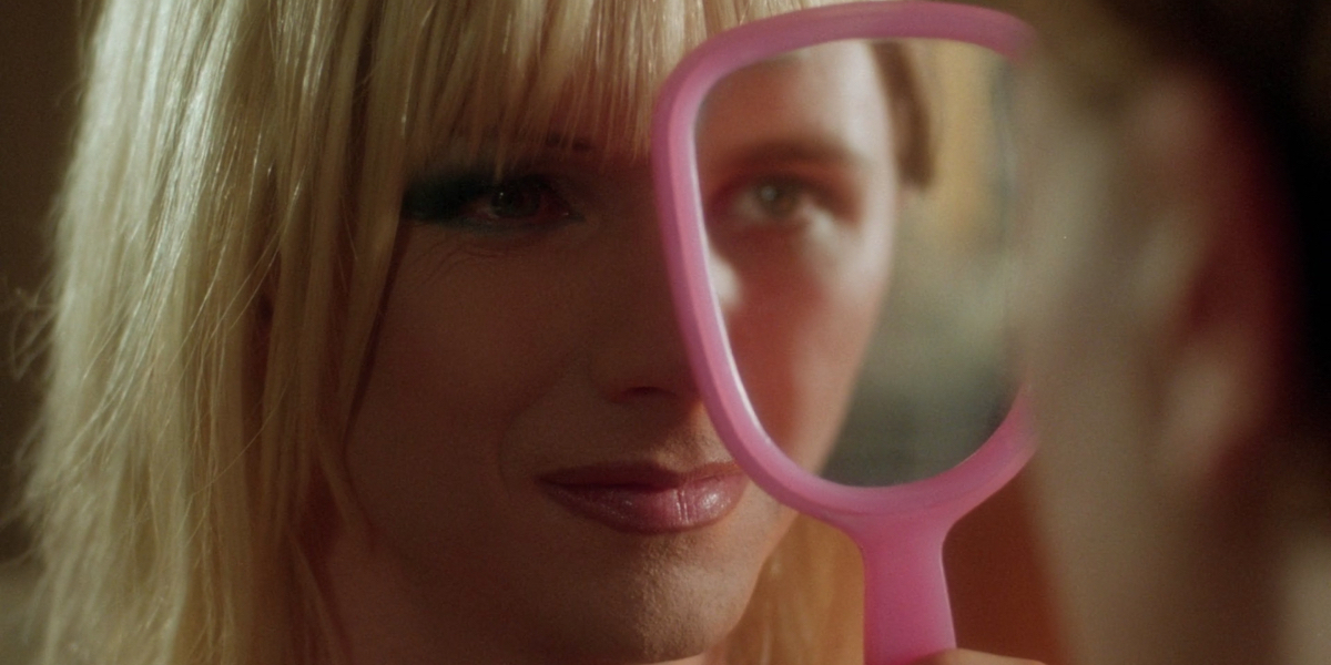 John Cameron Mitchell as Hedwig looks at Michael Pitt as Tommy Gnosis. Tommy holds up a pink mirror covering half of Hedwig's face so his face appears to complete hers.