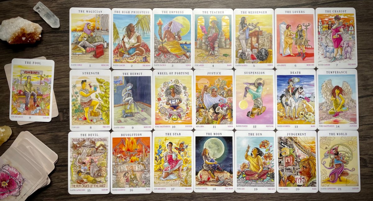 All 22 cards of the major arcana, laid out in three lines of seven cards each. The Fool card is set to one side alongside pieces of clear quartz and citrine.