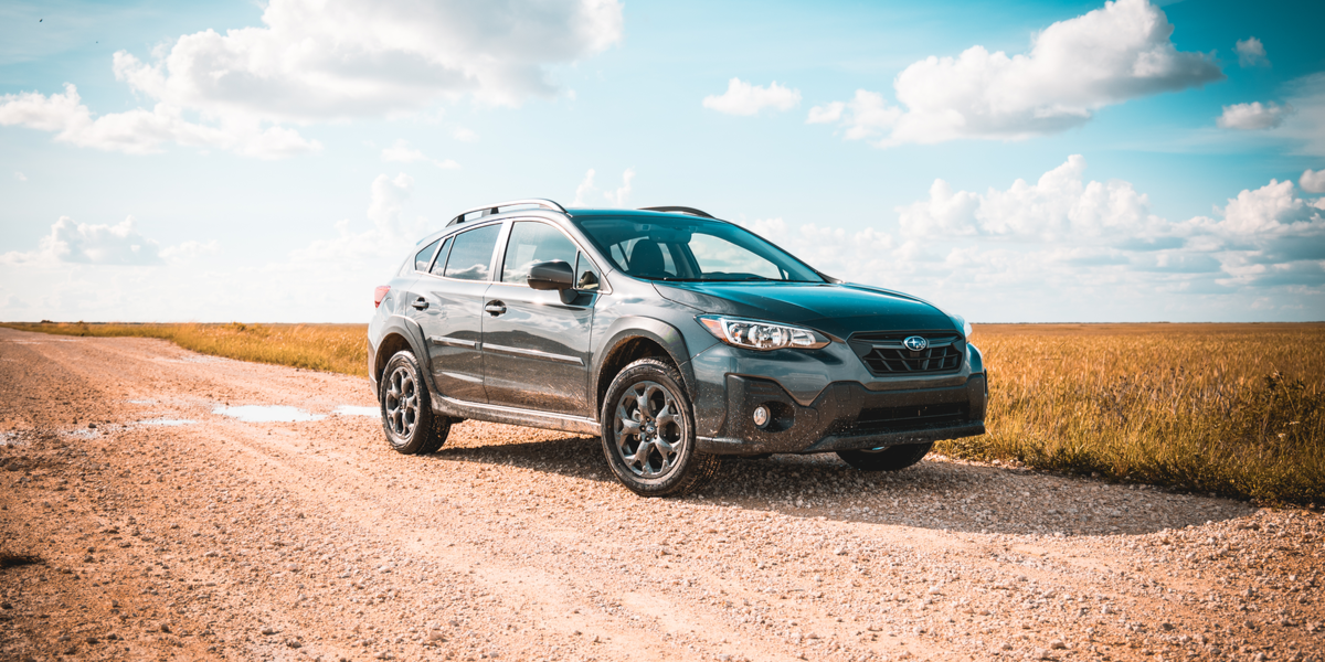 a black Subaru is parked on an open road with a blue sky with perfect white clouds above it