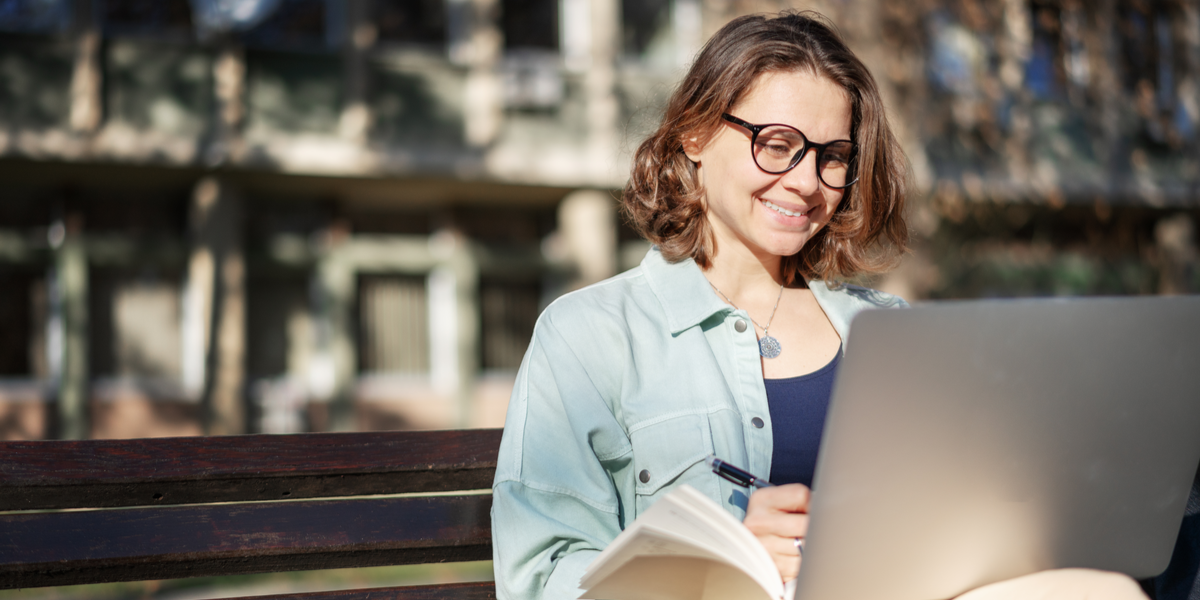 An image of a white woman with glasses smiling at her computer