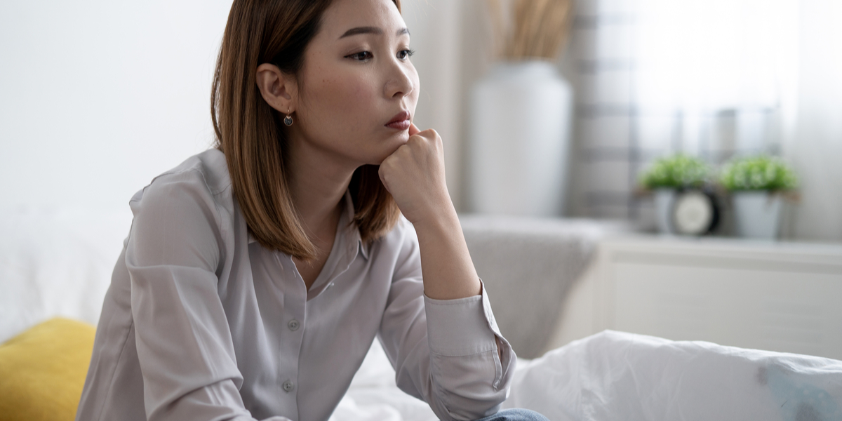 An Asian woman sits with her chin in her hands as she thinks pensively.