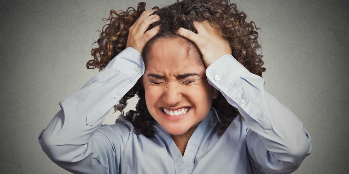frustrated woman is deciding if she should break up with her annoying girlfriend, she has dark curly hair clutches her head while making a pained expression