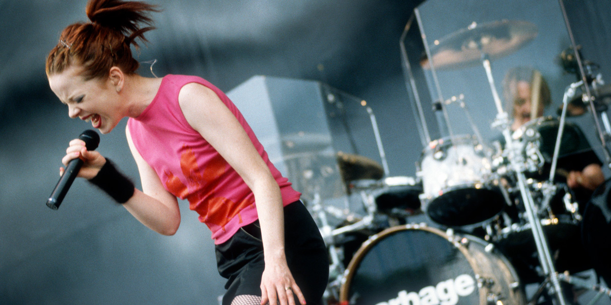 Shirley Manson rocks out on stage in a pink tank top and their hair pulled back into a ponytail.