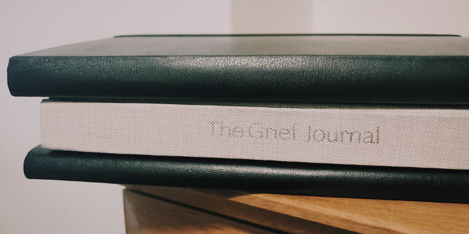 three stacked journals: the top and bottom journals are black and the middle journal is grey with the words The Grief Journal on the spine