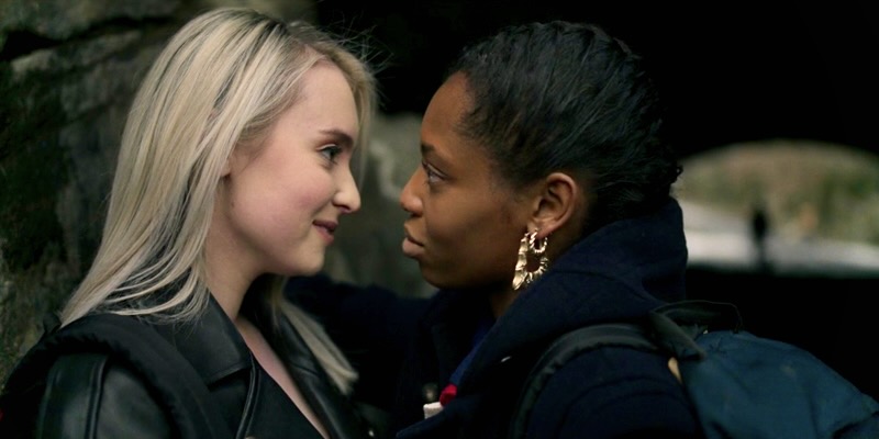 Two teenage girls, one white, Nicole, and one black, Jukebox, stare longingly at each other in a close up of their side profiles in a park in New York City.
