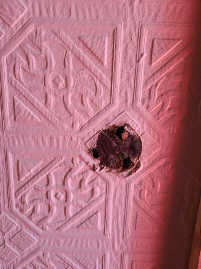 Stamped tin wallpaper gives way to a circular moment of wear and tear in the center, with smaller holes where a railing would have been installed.