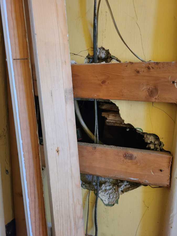 A hole in the wall where the doorbell chimer once lived, now a hole with wires coming out of it and two boards across it.