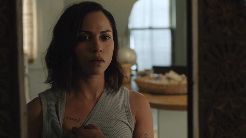 Jackie stares at herself, and her tattoo of Junior's name, in the mirror.