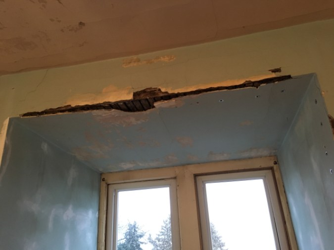 This is a photograph of a nook in Nicole's house in need of repair. Some plaster on a corner is falling off the wooden lath. The paint is patchy and there are a quite a few minor holes and cracks as well.