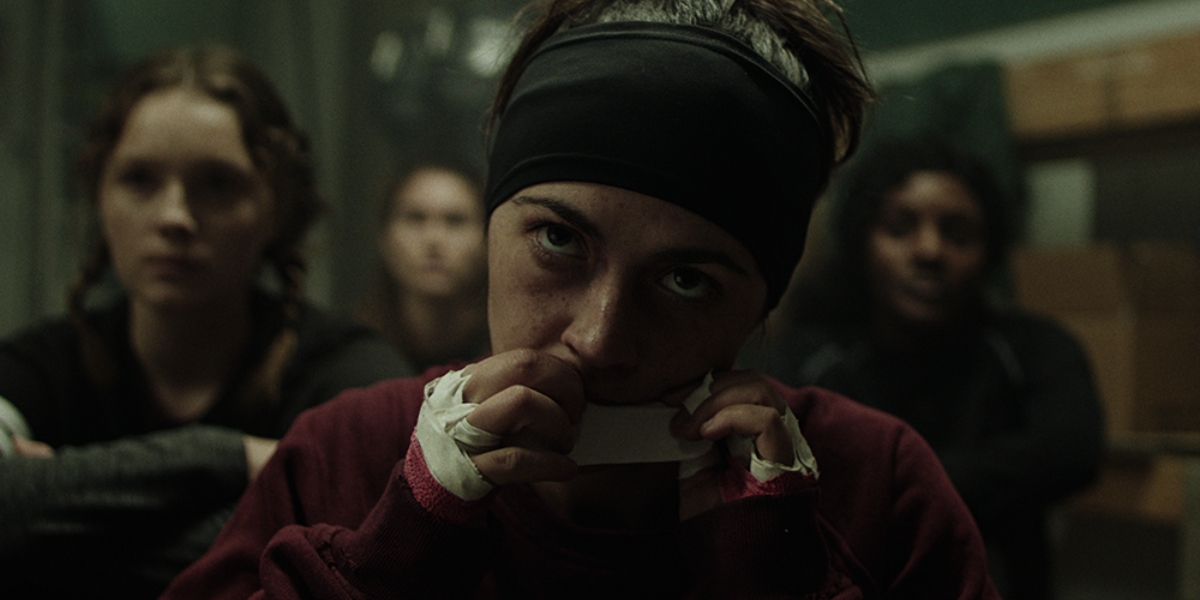 Isabelle Fuhrman as Alex Dall tears a piece of athletic tape with her teeth.