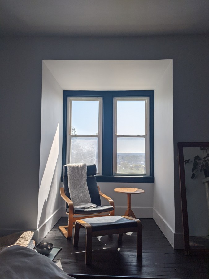 A photograph of the nook, all painted and repaired! Sunlight streams in across an ikea chair, ottoman and side table we found in the garbage!